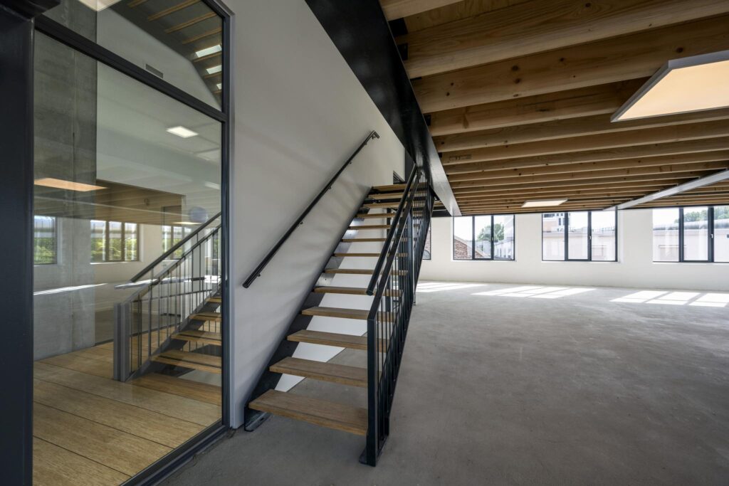 Modern empty office space on Paul van Vlissingenstraat with wooden ceiling beams, large windows, and a steel staircase.